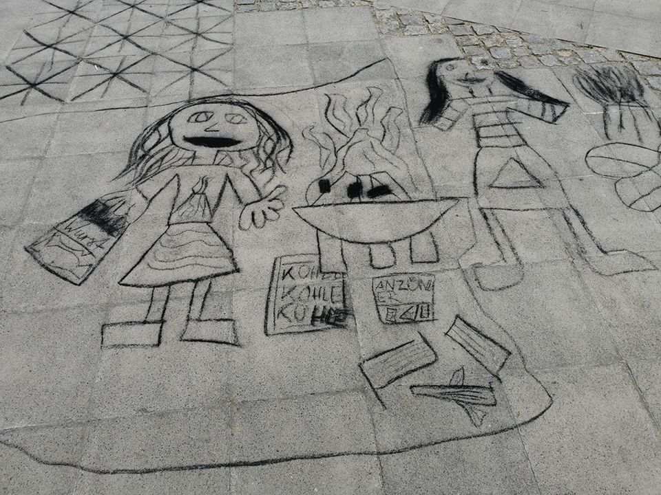 Zeichnung auf dem Bürgersteig mit Kindern die ein Lagerfeuer machen.